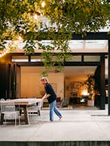 Woman adjusts patio furniture outside living room with floor-to-ceiling folding glass doors in midcentury home in Columbus, Ohio, renovated by GRA+D, Greg Dutton of Midland architecture and Ashley Sargent Price.