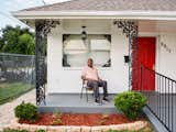 Man sits outside home in New Orleans, Louisiana, made of white-painted brick.