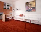 Retro interior with red shag carpet, white leather couch, floor lamps with translucent black glass shades, wood cabinetry, whicker chairs, and metal and glass coffee table.