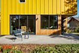Blue furniture on concrete patio pathway outside backyard ADU in Saint Paul, Minnesota, by Christopher Strom Architects with bright yellow painted wood cladding.