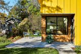 Blue furniture on concrete patio pathway outside backyard ADU in Saint Paul, Minnesota, by Christopher Strom Architects with bright yellow painted wood cladding.