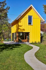 Concrete pathway leads to backyard ADU in Saint Paul, Minnesota, by Christopher Strom Architects with bright yellow painted wood cladding and steeped pitch roof.