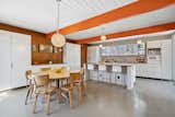 Bright orange beams stretch into the updated kitchen, providing a burst of color against the white cabinetry, wood-paneled walls, and period lighting.