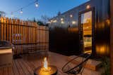aux box model 240 with black steel cladding and backyard wood deck with grill, hanging lights, fire pit, patio furniture, and wood fence.