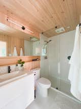 Bathroom of aux box model 240 prefab prefabricated home with white two-piece toilet, white wood laminate cabinetry, and pine-clad walls and ceiling.