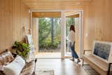 Woman opens floor-to-ceiling glass door from pine-clad living room of aux box model 240 prefab prefabricated home with covered wood deck.