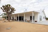 the outside of a white adobe home, a woman in a hammock with a dog underneath her