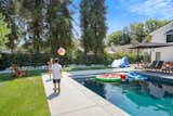Children play ball beside pool behind pool and California home.
