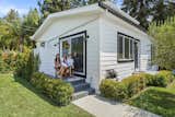 Family sits outside on covered patio of Villa prefab prefabricated ADU small home with fiber cement lap siding, asphalt gable roof, and clerestory windows in California backyard.
