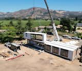 Crane lifts white metal clad unit of Connect Homes prefab prefabricated Designer Series home house onto construction site in California.