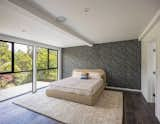 second-story bedroom in Connect Homes prefab prefabricated Designer Series home house in Walnut Creek, California, with black geometric wallpaper, upholstered bedframe and headboard, beige rug, dark wood floors, and floor-to-ceiling glass windows.