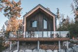 Cedar-sided, glulam prefab prefabricated home by Blend Projects with large deck with glass-paneled railing sits on hillside in British Columbia, Canada.