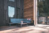 Sofa cushions site on wood paneled and steel framed bench outside cedar-sided, glulam prefab prefabricated home by Blend Projects with large wood deck in British Columbia, Canada.