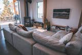 Living room with light grey beige sectional sofa and wood burning stove in cedar-sided, glulam prefab prefabricated home by Blend Projects with large deck and glass-paneled railing in British Columbia, Canada.