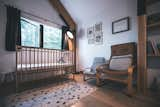 Child's bedroom with wooden crib cot bed, rocking chairs, tall black floor lamp, pitched ceiling, and monochrome polka-dot rug in cedar-sided, glulam prefab prefabricated home by Blend Projects in British Columbia, Canada.