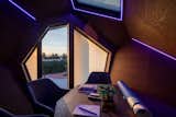 Faceted dark wood-paneled interior of Aluminum-clad  prefab prefabricated Cyber pebble pod outdoor workstation by Hello Wood with purple led lights, conference tables, and fabric chairs.