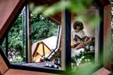 Woman sits on raised plywood bench reading a book in pine timber-clad  prefab prefabricated pebble pod outdoor workstation by Hello Wood.