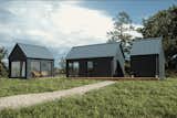 MyCabin suite of prefab prefabricated units including the tiny house My Milla 25, My Milla Long, My Galia sauna, and My Kalmus ADU studio office workspace with black spruce cladding and blackened standing seam metal roofs seen across grass yard  and gravel walkway.
