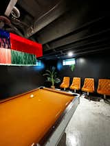 The pool table in the basement features a bespoke chandelier created in collaboration with New Orleans-based lighting designer Mimi Girouard. The "dive bar" lounge aesthetic is enhanced with walls painted in a Sherwin Williams semi-gloss, Tricorn Black.