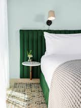 a green padded headboard, white sheets, a grey waffled blanket on a bed