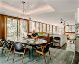 Rick Cook sits at oval table with medium toned wood chairs upholstered in black leather, green and grey rug, and large floor-to-ceiling glass windows in dining room of house in Palisades New York by Charles P Winter renovated by CookFox.