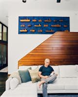 Rick Cook sits on white Jasper sofa in living room with dark wood flooring and blue carpet in house in Palisades New York by Charles P Winter renovated by CookFox.