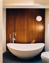 Vessel white bathtub sits in bathroom with closet enclosed by large, floor-to-ceiling dark wood doors, blue tile flooring, and white tile walls in house in Palisades New York by Charles P Winter renovated by Rick Cook Fox CookFox.