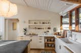 Kitchen with concrete topped island, white counters, light wood and white cabinetry, white sink and faucet, translucent lantern pendant light, light hard wood floors, shed ceiling, and white-painted brick walls.