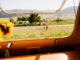 View of couple running across field from kitchen window of white Argosy airstream from 1975 renovated by Caroline Burke and Riley Haakon.