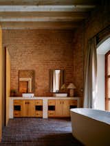 Bathroom in an 1800s brick structure in Todos Santos, Baja California, Mexico, renovated and expanded by Ernesto Kut Gomez, Ellen Odegaard, and Yashar Yektajo with white vessel bathtub, custom wood millwork cabinetry, exposed brick walls, and wood ceiling.