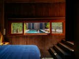 Bedroom in concrete tower added to an 1800s brick structure in Todos Santos, Baja California, Mexico, renovated and expanded by Ernesto Kut Gomez, Ellen Odegaard, and Yashar Yektajo with long wood-framed window looking out over woman swimming in pool.