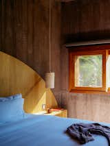 Bedroom in concrete tower added to an 1800s brick structure in Todos Santos, Baja California, Mexico, renovated and expanded by Ernesto Kut Gomez, Ellen Odegaard, and Yashar Yektajo with yellow wood headboard and built-in nightstand and whicker pendant light.