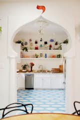 Kitchen with white, walls and cabinetry, stone granite countertops, and sky blue floor tiling patterned with white circles seen through an arabesque, oriental archway in a house in Bywater, New Orleans, renovated by Mitchell Kulkin and John Cameron Mitchell.