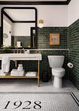 The bathrooms channel feature green wall tile, black crown molding, brass fixtures, and marble flooring centered with a basket-weave pattern and the 1928 logo.
