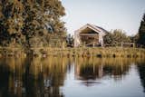 Tiny home micro home LOVT in Germany with dark wood cladding, large panoramic window, and metal roof sits in forest beside pond lake.