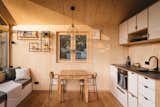 Interior living room, dining room, and kitchen of tiny home micro home LOVT in Germany with sectional bench daybed reading nook, medium-toned hard wood floors, spruce walls, pitched roof,  and white kitchen cabinetry.
