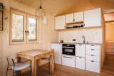 Interior dining room, and kitchen of tiny home micro home LOVT in Germany with medium-toned hard wood floors, spruce walls, pitched roof,  and white kitchen cabinetry.
