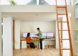 Couple works at desk in accessory dwelling unit ADU by Mai Tran and Le Pham in Albany, California CA with white walls, pitched ceiling, in-built shelves, and light wooden floors.