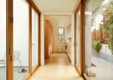 Hallway in accessory dwelling unit ADU by Mai Tran and Le Pham in Albany, California CA with floor-to-ceiling folding accordion glass doors ends in kitchen with light wood floors, white cabinetry, and white countertops.