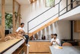 Couple talk in kitchen as one drinks coffee at concrete topped dining table and the other pets golden retriever dog on mezzanine raised split level walkway in home outside Puerto Varas, Chile, designed by Camilo Fuentealba and Eduardo Díaz of Estudio Sur.