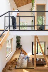 Couple talk to each other in double-height living room as one sits in ground level living room and the other leans on railing of on second-story landing in home outside Puerto Varas, Chile, designed by Camilo Fuentealba and Eduardo Díaz of Estudio Sur.