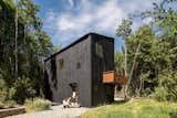 Home outside Puerto Varas, Chile, designed by Camilo Fuentealba and Eduardo Díaz of Estudio Sur, with two stories, blackened wood cladding, cantilevered balcony, and gravel driveway sits in forest.