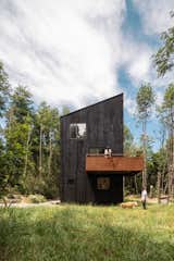 Home outside Puerto Varas, Chile, designed by Camilo Fuentealba and Eduardo Díaz of Estudio Sur, with two stories, blackened wood cladding, cantilevered balcony, and gravel driveway sits in forest. 