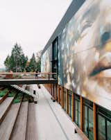 A 3,000-square-foot mural by artist Guido van Helten overlooks benched seating leading down to basement and bridge leading to the entrance of PorchLight Eastgate shelter in Bellevue, Washington WA, designed by Joshua P. LaFreniere, JPL-A, Block Architects, Jennifer LaFreniere, and Rex Hohlbein.