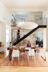 Emilie Taylor and Seth Welty of design firm Colectivo design their own house in the Black Pearl neighborhood of New Orleans, Louisiana LA, with double-height living and dining room with light hardwood flooring, red coral rug, black aluminum framed table with medium-toned wood table top, white chairs, large fabric pendant light, black metal staircase, slatted wood screen, and white walls.