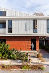 Emilie Taylor and Seth Welty of design firm Colectivo design their own house in the Black Pearl neighborhood of New Orleans, Louisiana LA, with angled roof, white metal and terracotta cladding, large bushes in landscaped front lawn, and gravel driveway.