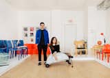 Portrait of David Barsoum and Niky Sampedro in their store Carefully Picked in Chicago, Illinois IL, with light wood floor and white podiums holding curving blue and red chairs, a light wood chair with green cushion, and a set of nesting coffee tables.
