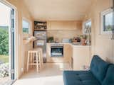 Interior of Norske Mikrohus tiny house micro house tind adu accessory dwelling unit prefab prefabricated in Norway with birch veneer walls, birch veneer ceiling, birch veneer floors, lofted bedroom with ladder, white counters, and floor to ceiling glass folding door window.