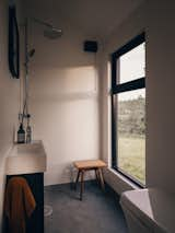 Interior bathroom wetroom of Norske Mikrohus tiny house micro house rast adu accessory dwelling unit prefab prefabricated in Norway with shower, dark vinyl floors, large window, stool, and one-piece toilet.