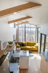 Interior of Fritz Tiny Home Halcyon model with medium-toned wood floors and ceiling, white and dark-toned millwork, lofted bedroom, white kitchen cabinets, yellow sofa, and concrete countertops.